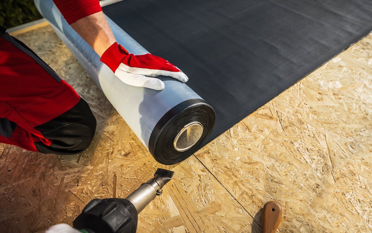 Roofing worker preparing to lay an EPDM rubber membrane over a flat roof deck