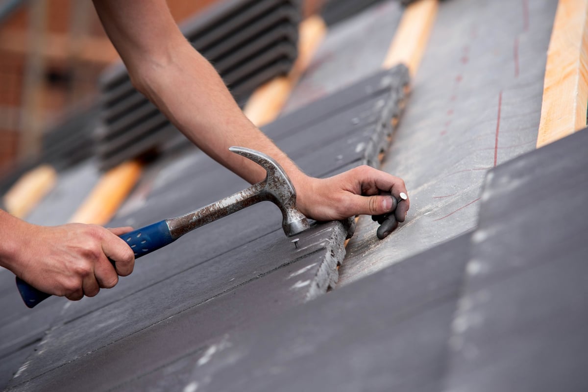 Roofer's hands placing and aligning clay roof tiles on a pitched roof