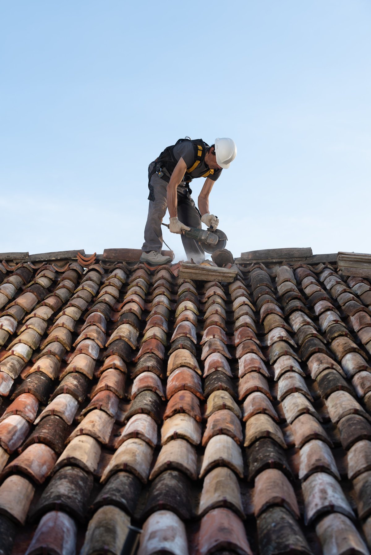 Roofer working safely on a residential clay tile roof, secured with a harness